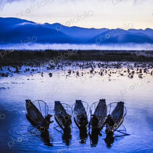 A group of fishermen on Lake Inle at dusk, mist rising from the water.