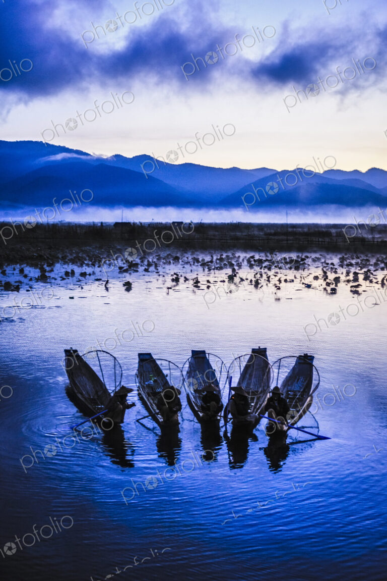 A group of fishermen on Lake Inle at dusk, mist rising from the water.