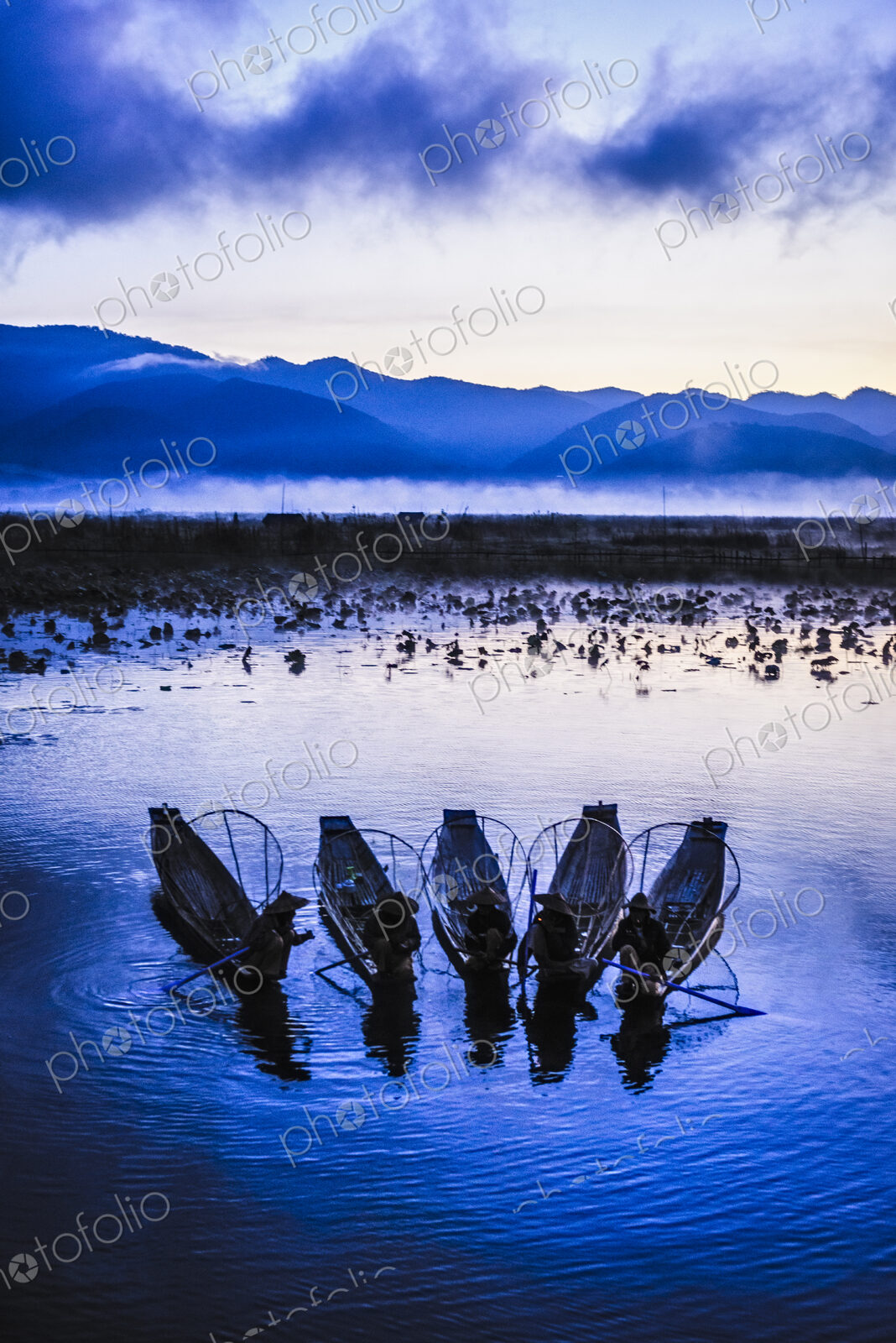 A group of fishermen on Lake Inle at dusk, mist rising from the water.