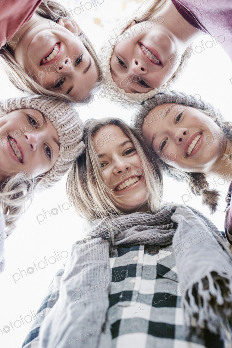 A group of five teenage girls outdoors in woolly hats and scarves.
