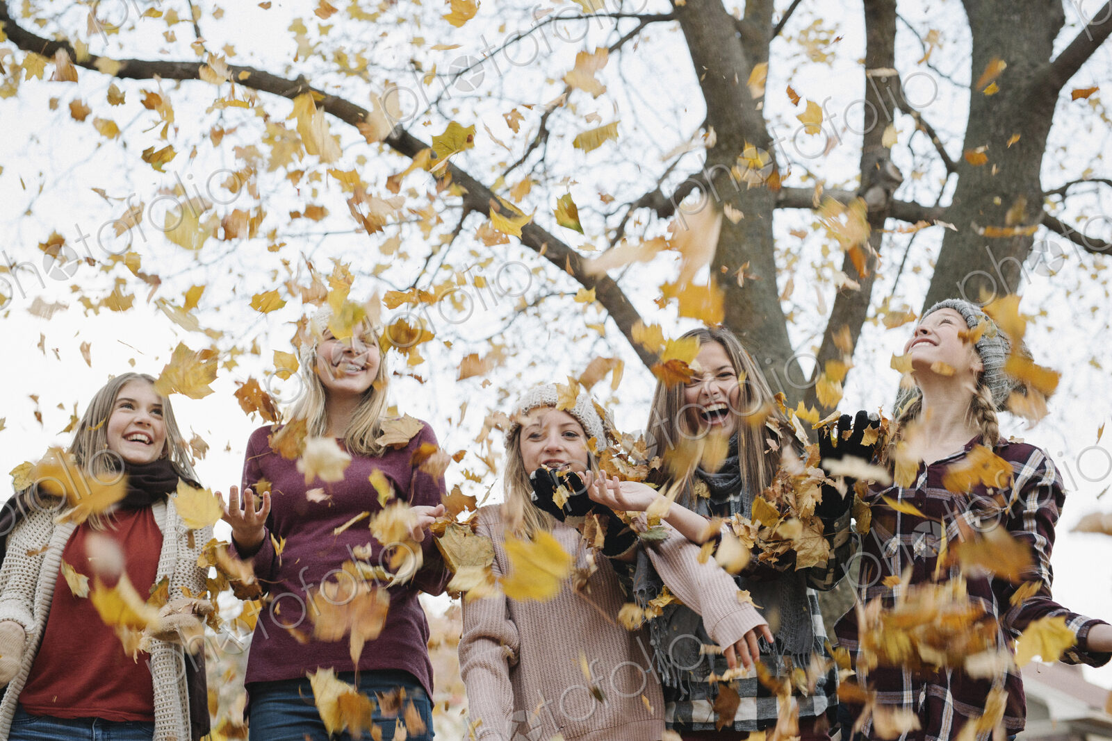A group of five teenage girls throwing autumn leaves in the air.