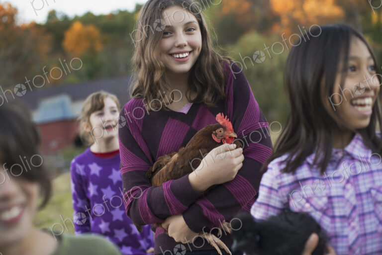 A group of four children in a group, two girls holding chickens, carrying them. A…