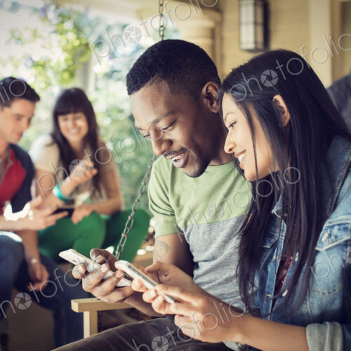 A group of friends, men and women at a house party, a couple checking their smart phones.