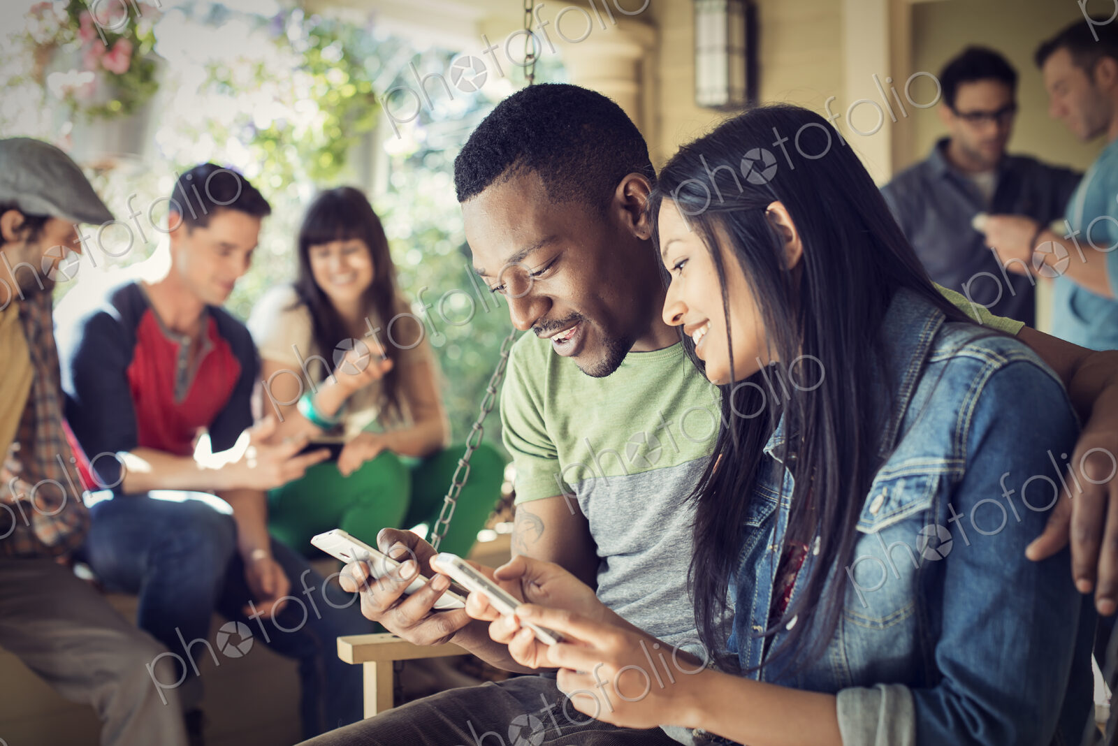 A group of friends, men and women at a house party, a couple checking their smart phones.