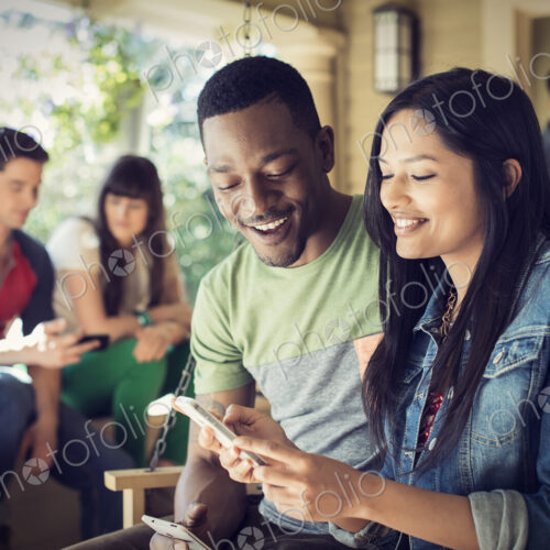 A group of friends, men and women at a house party, a woman holding a smart phone.