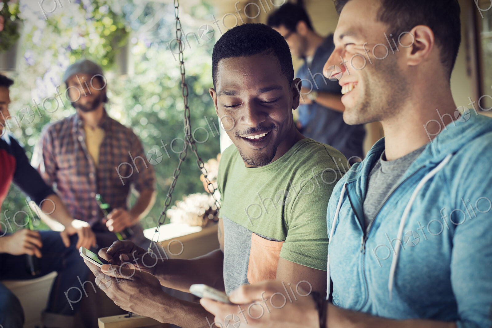 A group of friends, men and women at a house party, two men looking at their smart phones.