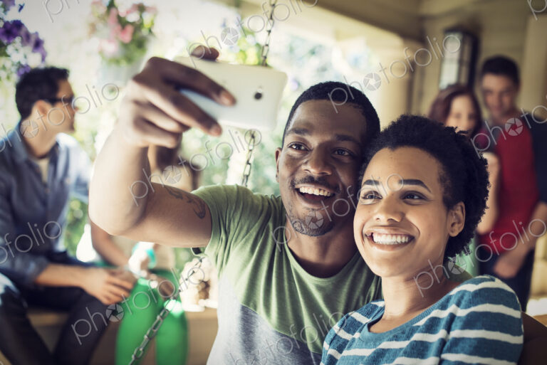 A group of friends, men and women at a house party. A cpuple taking a selfie.