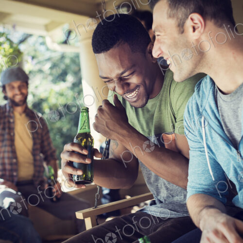 A group of friends, men and women at a house party. Two men laughing.