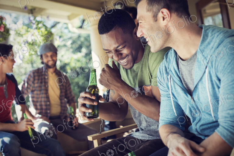 A group of friends, men and women at a house party. Two men laughing.