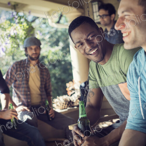 A group of friends, men and women at a house party. Two men laughing together.