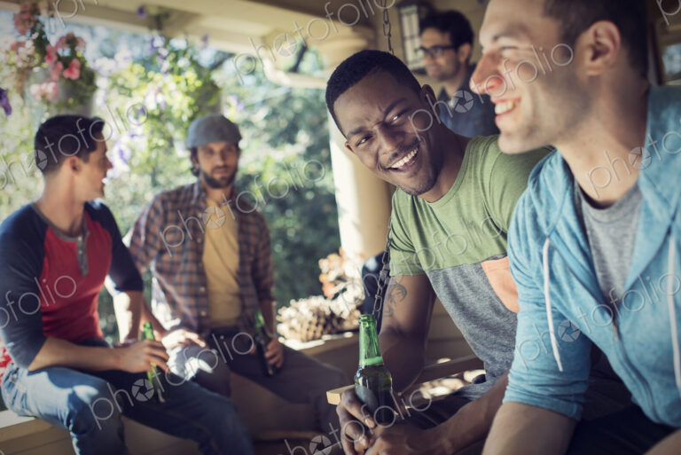 A group of friends, men and women at a house party. Two men laughing together.