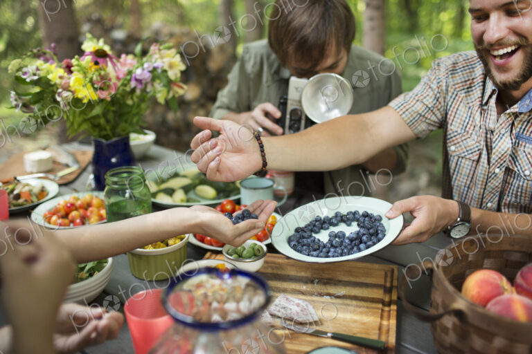 A group of friends outdoors sharing dishes of fresh fruits and salads.