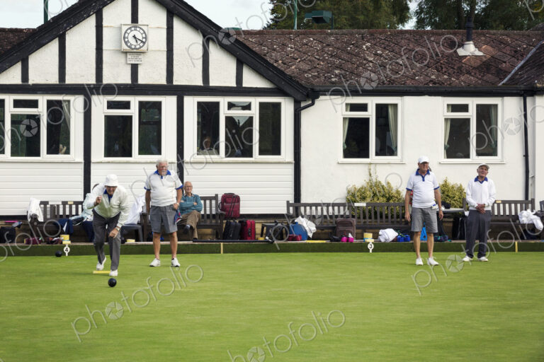 A group of lawns bowls players by a clubhouse, preparing for play.