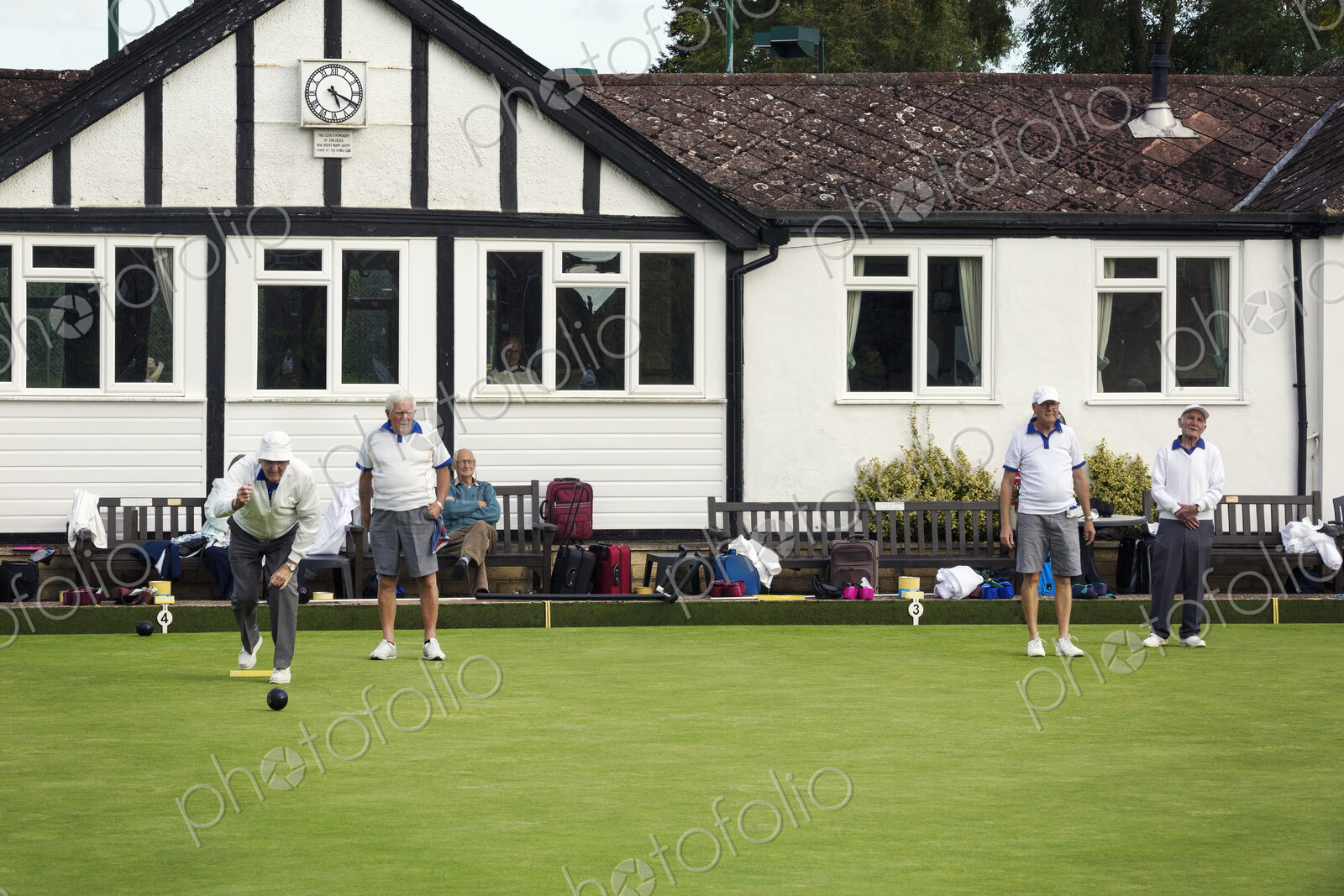 A group of lawns bowls players by a clubhouse, preparing for play.