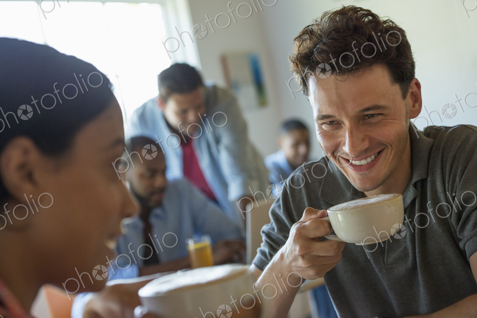 A group of men and women in a cafe, eating and drinking and enjoying each other’s company.