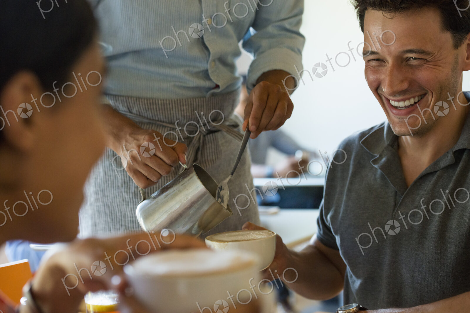 A group of men and women in a cafe, eating and drinking and enjoying each other’s company.