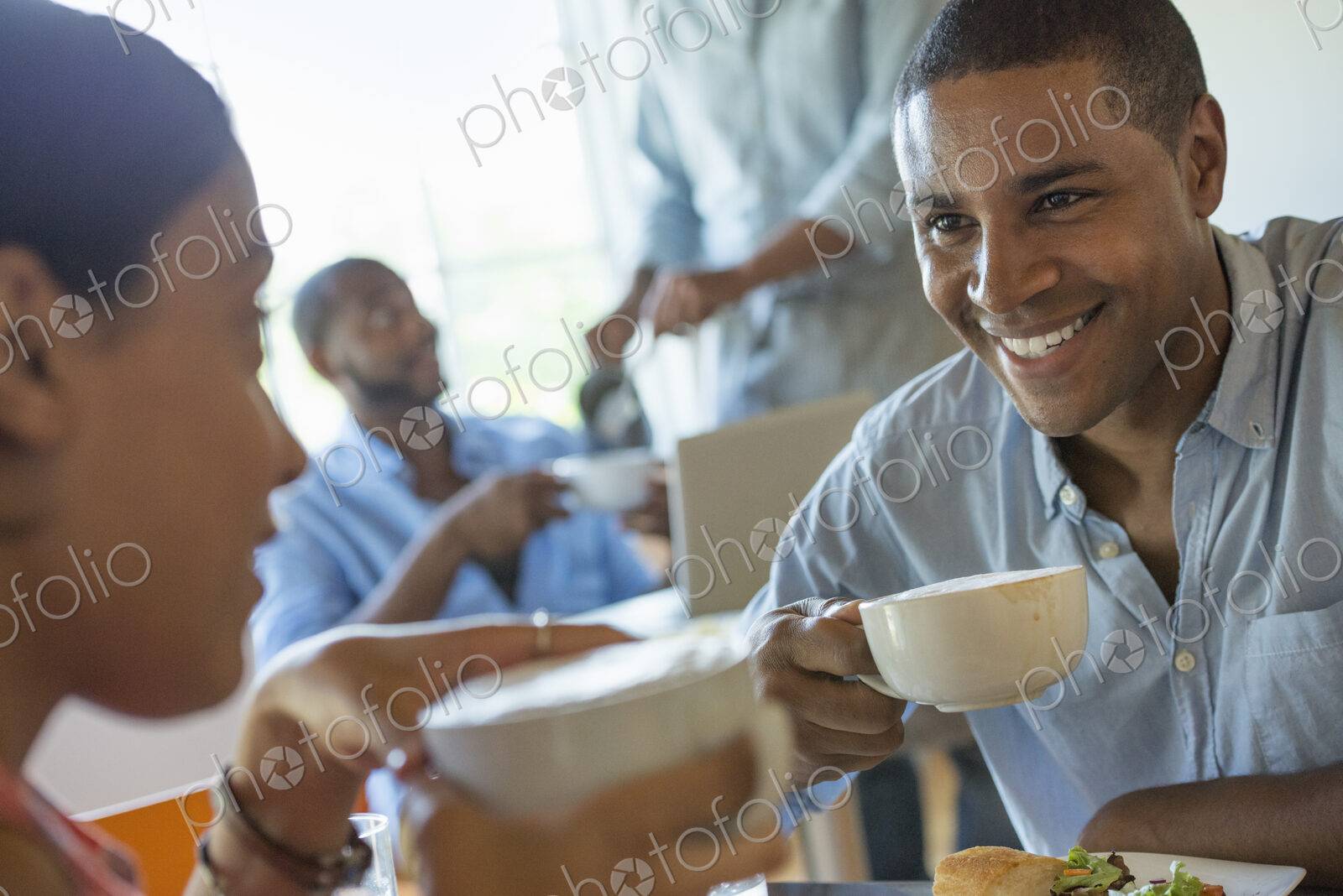 A group of men and women in a cafe, eating and drinking and enjoying each other’s company.