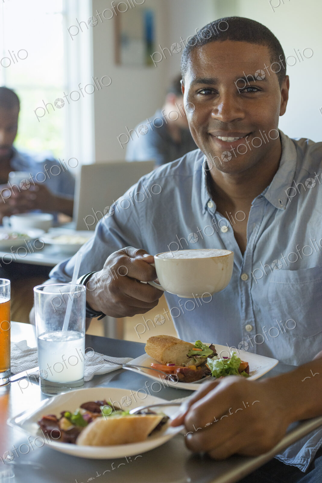 A group of men and women in a cafe, eating and drinking and enjoying each other’s company.