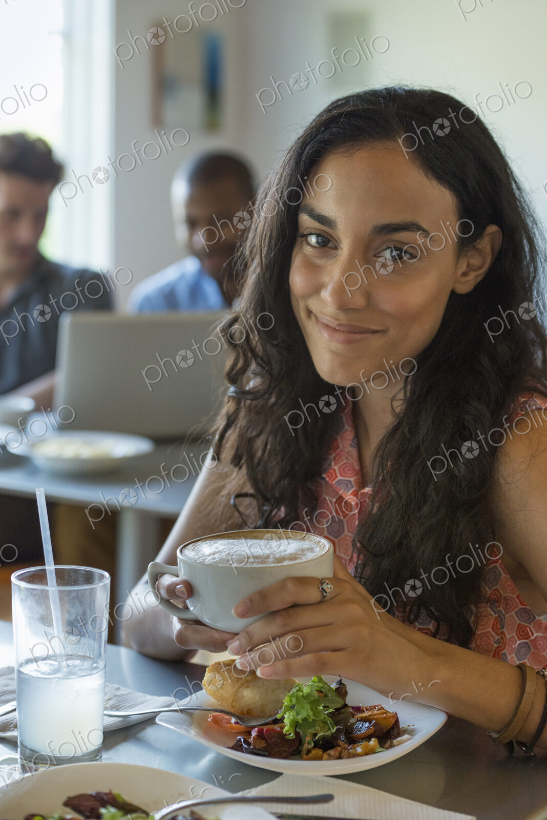 A group of men and women in a cafe, eating and drinking and enjoying each other’s company.