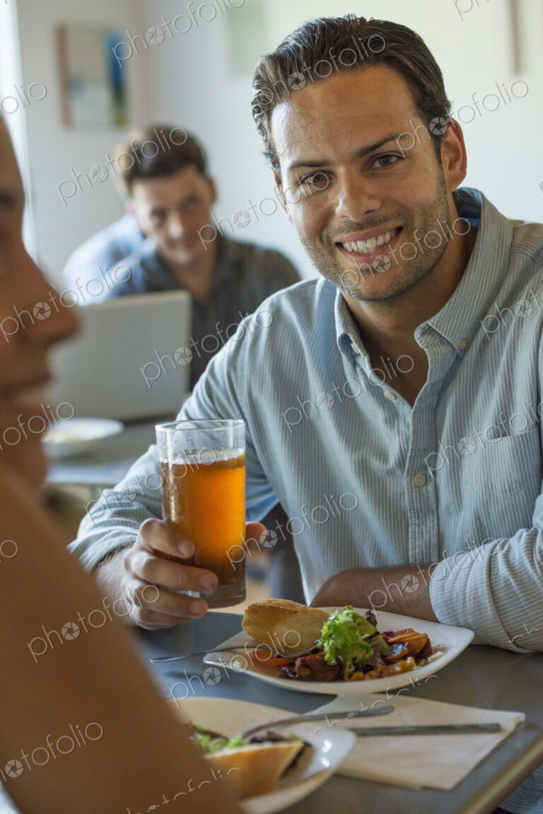 A group of men and women in a cafe, eating and drinking and enjoying each other's company.