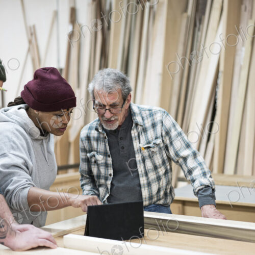 A group of mixed race carpenters discussing a project at a work station in a large…