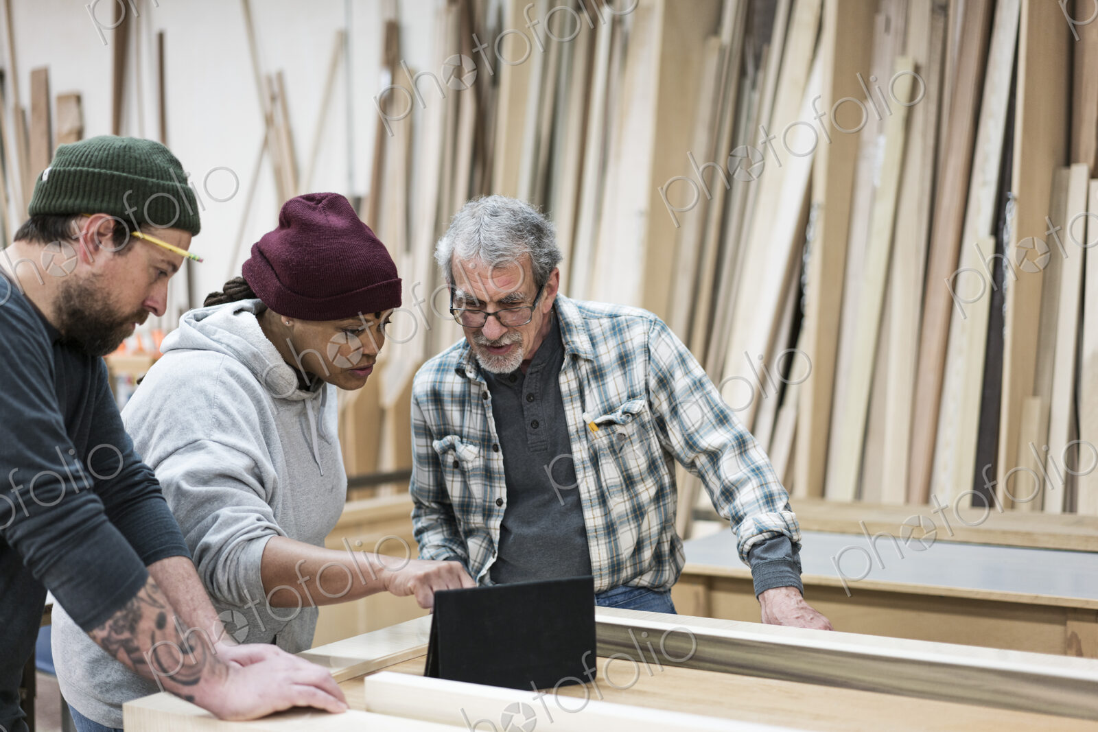 A group of mixed race carpenters discussing a project at a work station in a large…