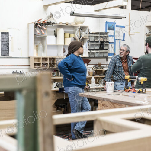 A group of mixed race carpenters discussing a project at a work station in a large…