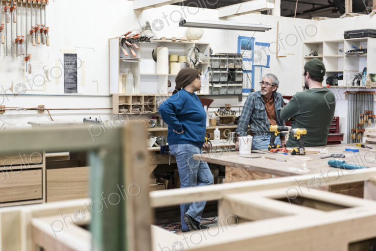 A group of mixed race carpenters discussing a project at a work station in a large…