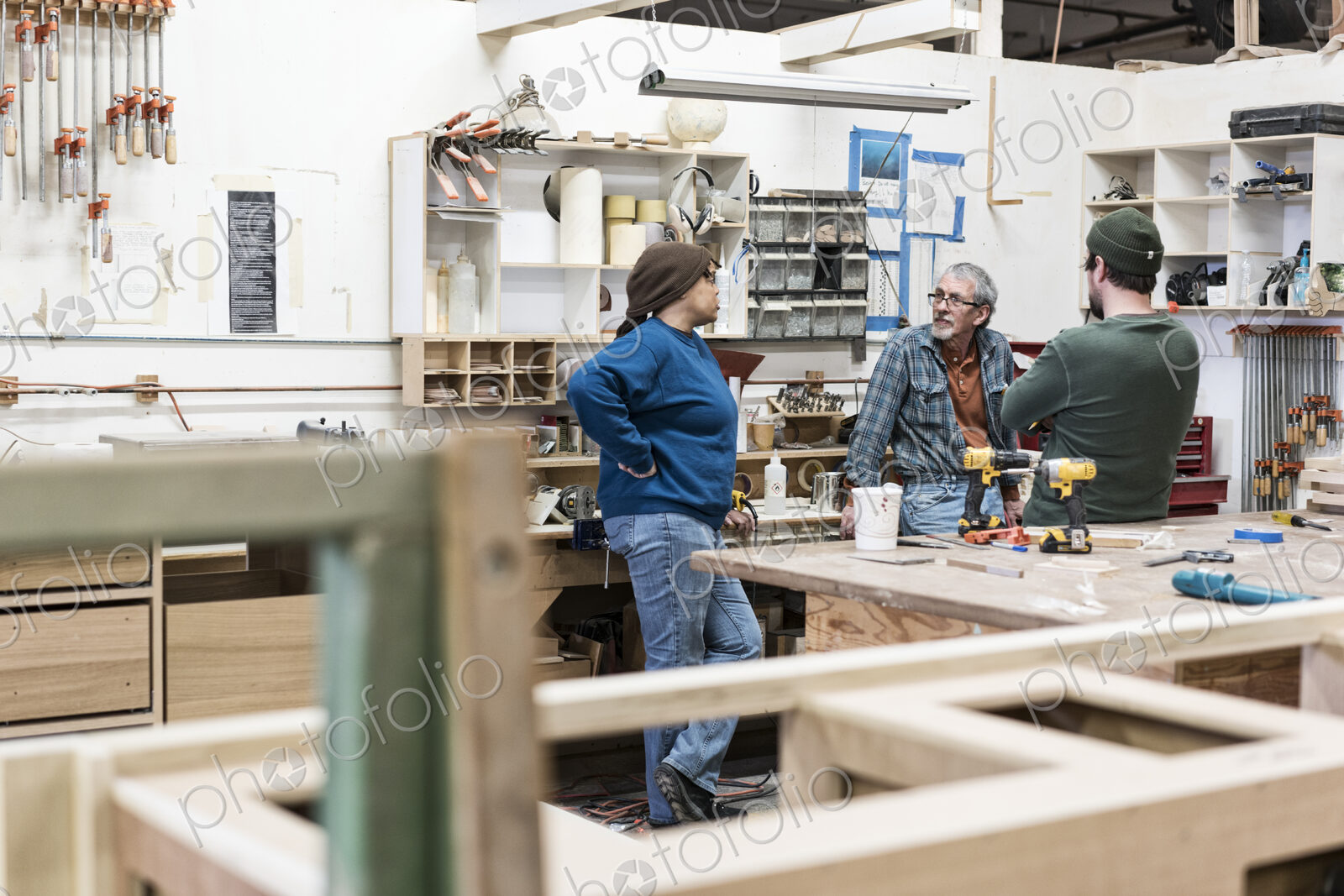 A group of mixed race carpenters discussing a project at a work station in a large…