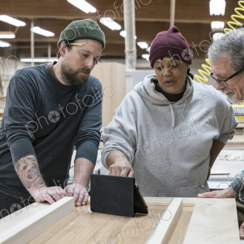 A group of mixed race carpenters discussing a project at a work station in a large…