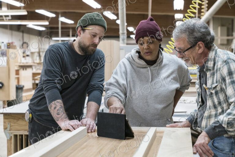 A group of mixed race carpenters discussing a project at a work station in a large…