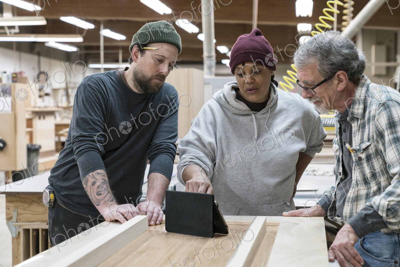 A group of mixed race carpenters discussing a project at a work station in a large…