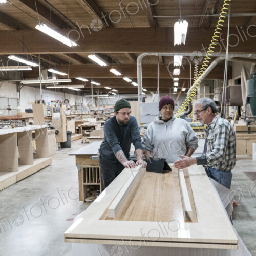 A group of mixed race carpenters discussing a project at a work station in a large…