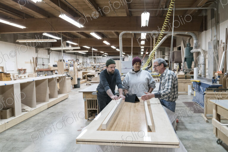 A group of mixed race carpenters discussing a project at a work station in a large…