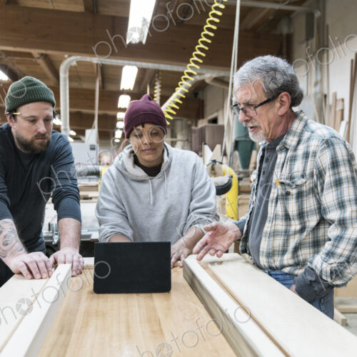 A group of mixed race carpenters discussing a project at a work station in a large…