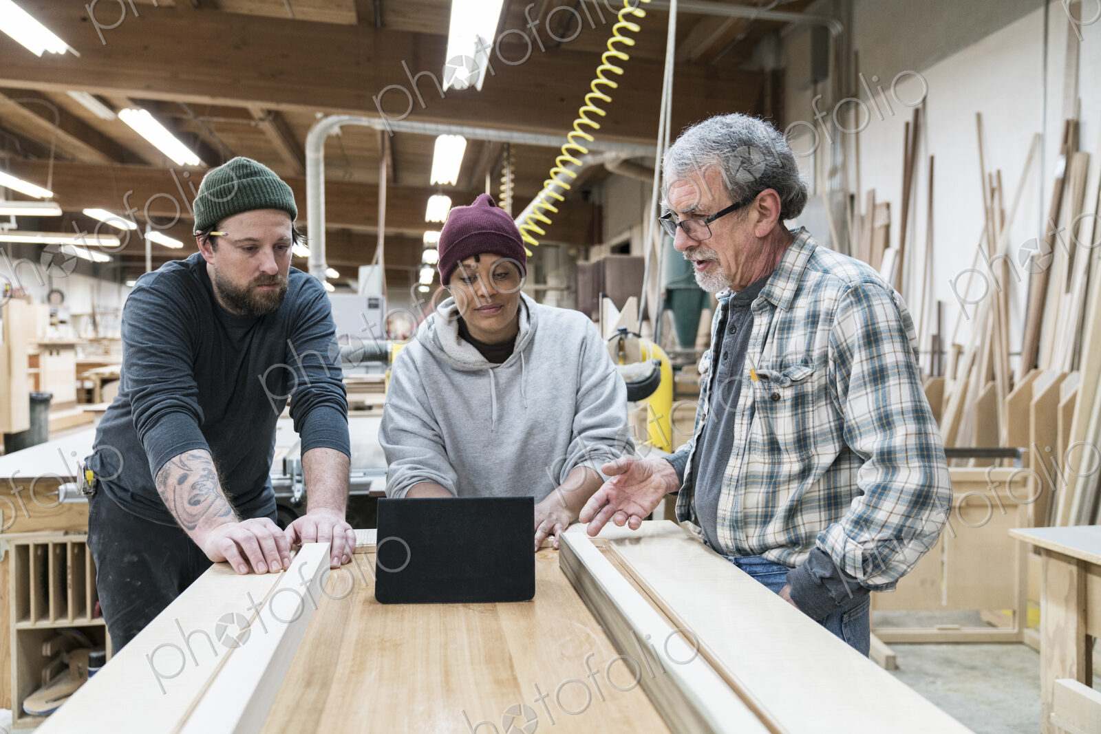 A group of mixed race carpenters discussing a project at a work station in a large…