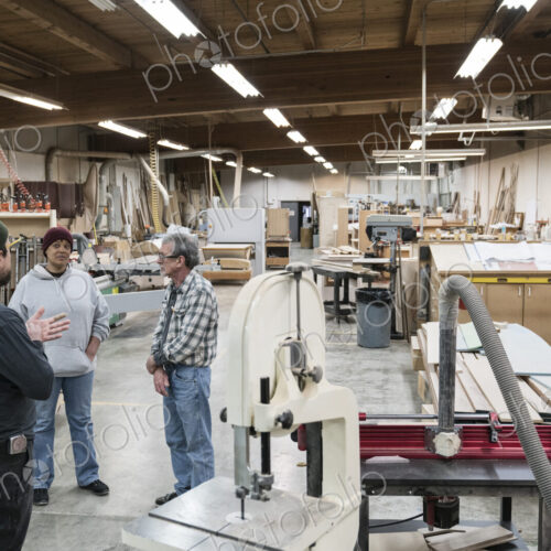 A group of mixed race carpenters discussing a project at a work station in a large… A group of mixed race carpenters discussing a project at a work station in a large…