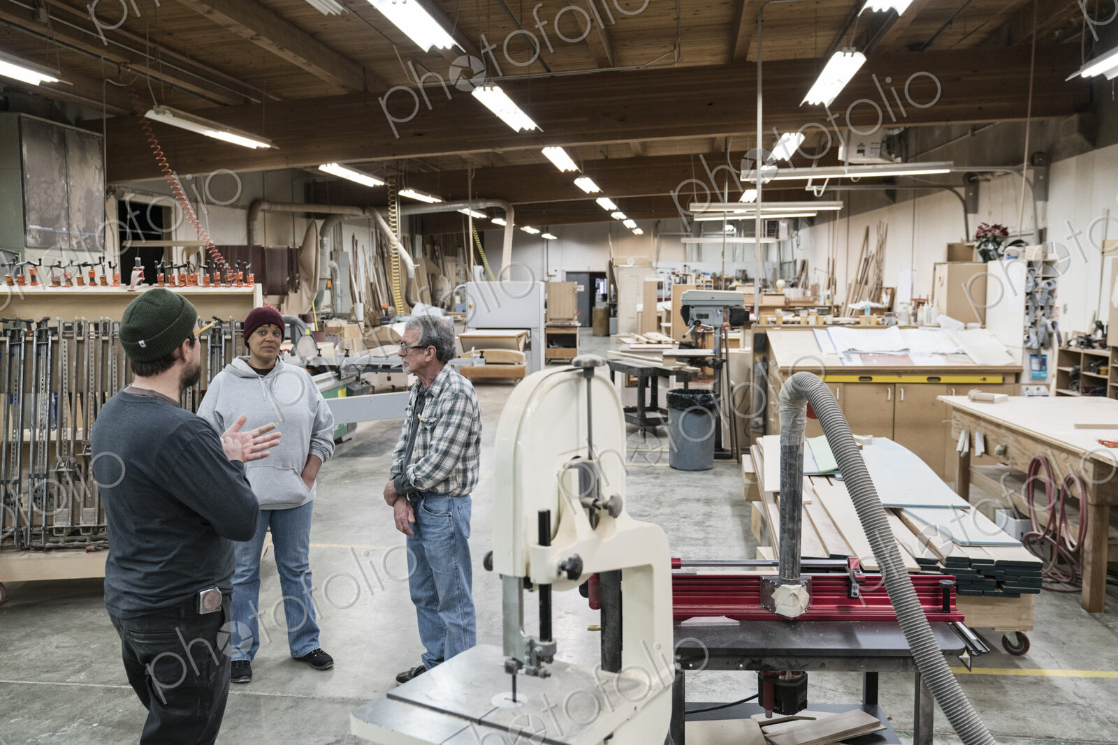 A group of mixed race carpenters discussing a project at a work station in a large…