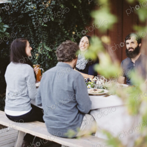 A group of people around a table in a garden. A celebration meal, with table settings…
