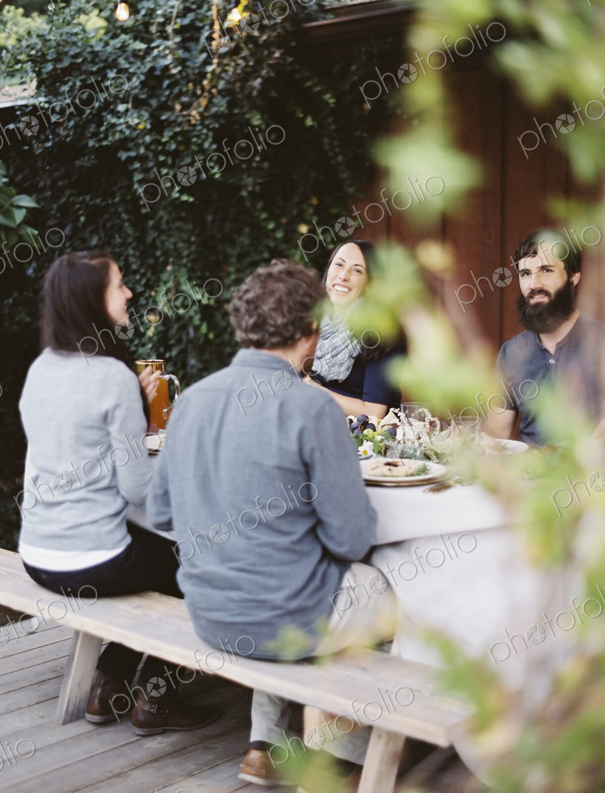 A group of people around a table in a garden. A celebration meal, with table settings…