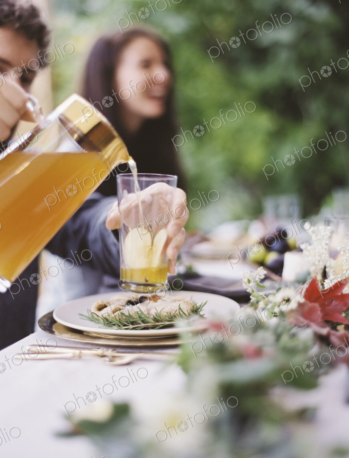 A group of people around a table in a garden. A celebration meal, with table settings…