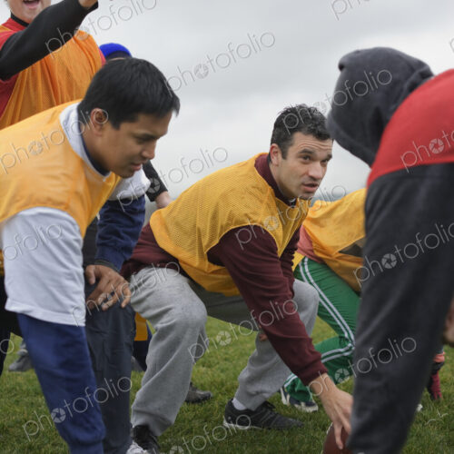 A group of people crouching, one playing quarterback for an non-contact flag football…