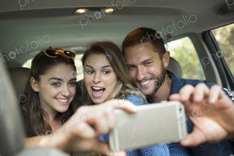 A group of people in a car, two women and a man taking a selfy.