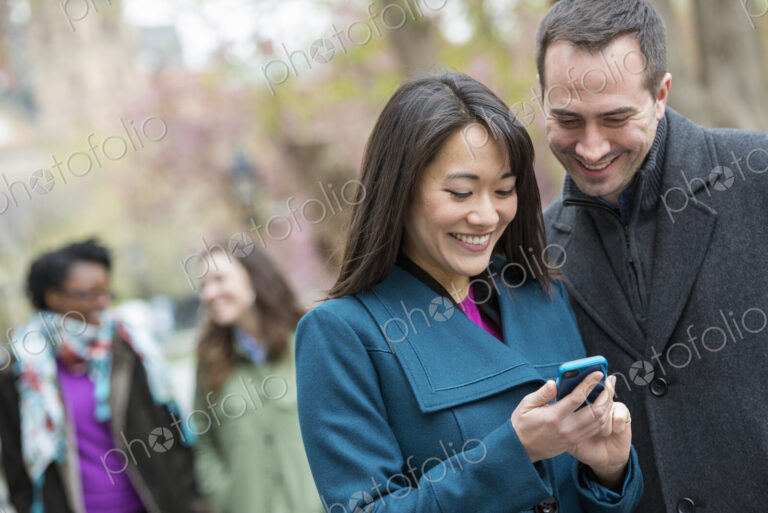 A group of people in a city park. A man in a grey coat, and a woman in a turquoise…