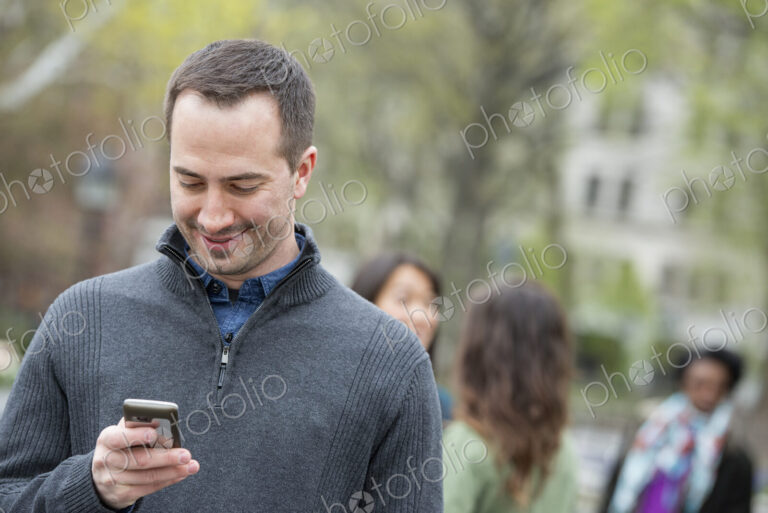 A group of people in a city park. A man in a grey sweater, checking his phone.