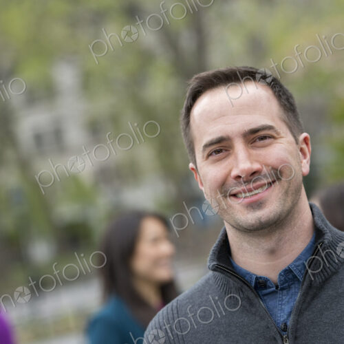 A group of people in a city park. A man in a grey sweater, smiling.