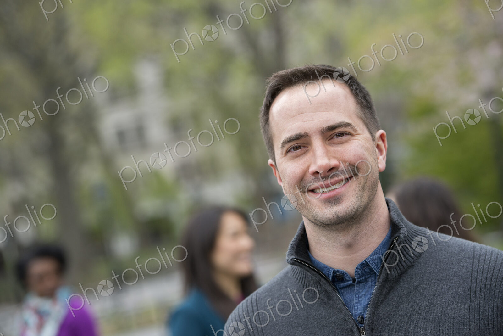 A group of people in a city park. A man in a grey sweater, smiling.