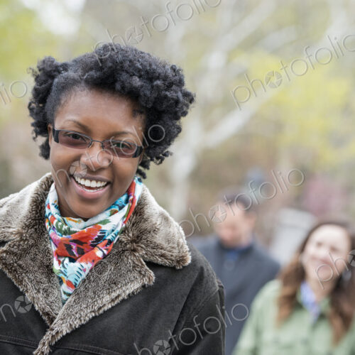 A group of people in a city park. A young woman in a coat with a large collar, smiling…