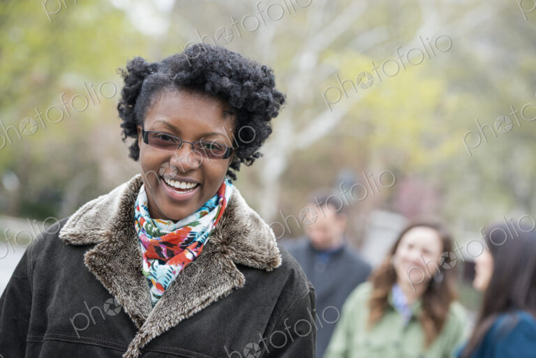 A group of people in a city park. A young woman in a coat with a large collar, smiling…