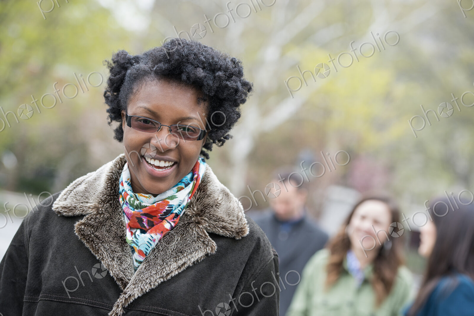 A group of people in a city park. A young woman in a coat with a large collar, smiling…